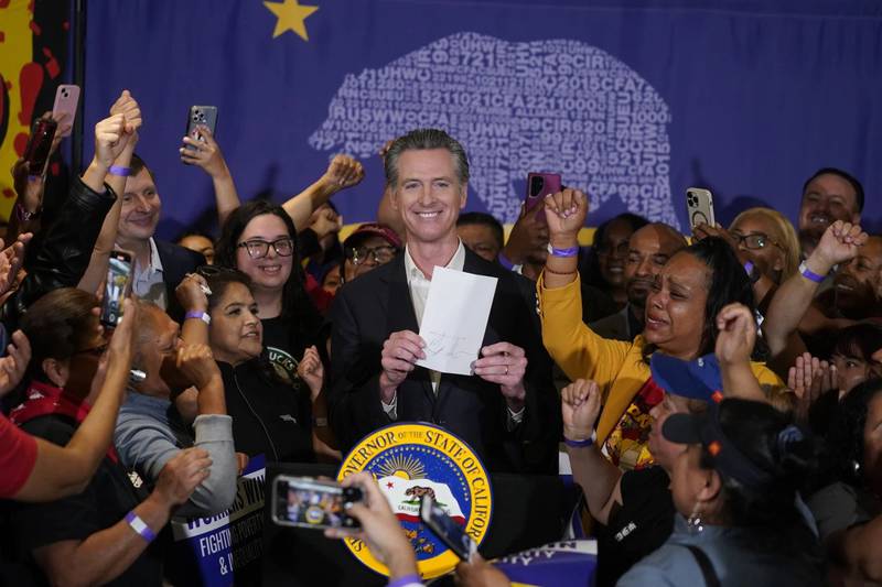 California Gov. Gavin Newsom signs the fast food bill surrounded by fast food workers at the SEIU Local 721 in Los Angeles. Anneisha Williams (right), who works at a Jack in the Box restaurant in southern California, celebrates.