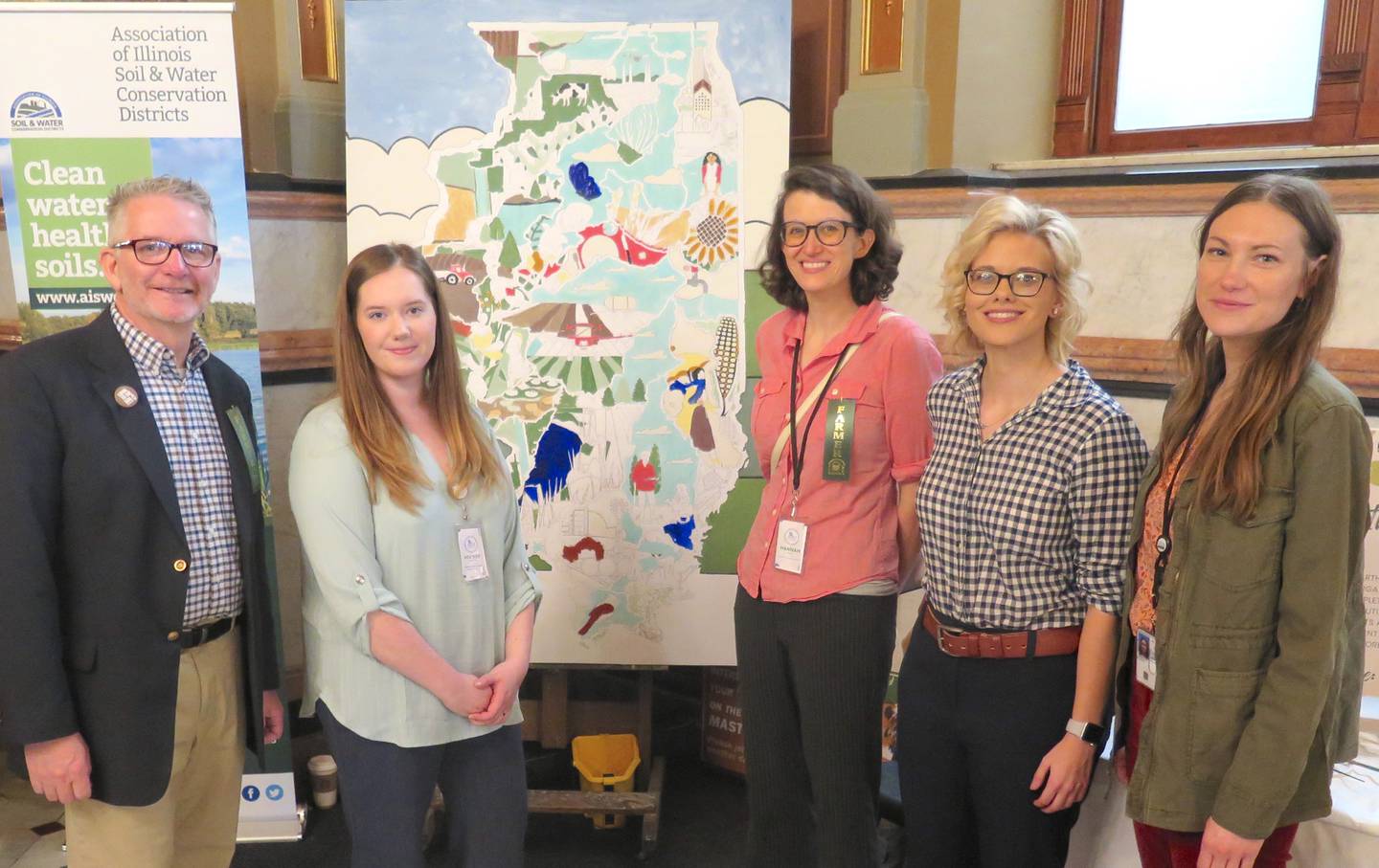 The Art and Science of Soil Health display featured near the main entrance of the Illinois Capitol Rotunda during Soil Health Week allowed visitors to use soil-based paints on a map of Illinois that showcases the state’s diversity of agriculture, watersheds and conservation. NRCS and SWCD conservation planners staffed the display. Featured at the booth during the March 6 lobby day included Michael Woods (from left), Association of Illinois Soil and Water Conservation Districts executive director; Heather VanTilburg, Boone County; Hannah Tomlin, Agroecology + Innovation Matters soil health outreach associate; Taylor Hartke, Clay County; and Alexis Zimmerlein, JoDaviess and Carroll counties.