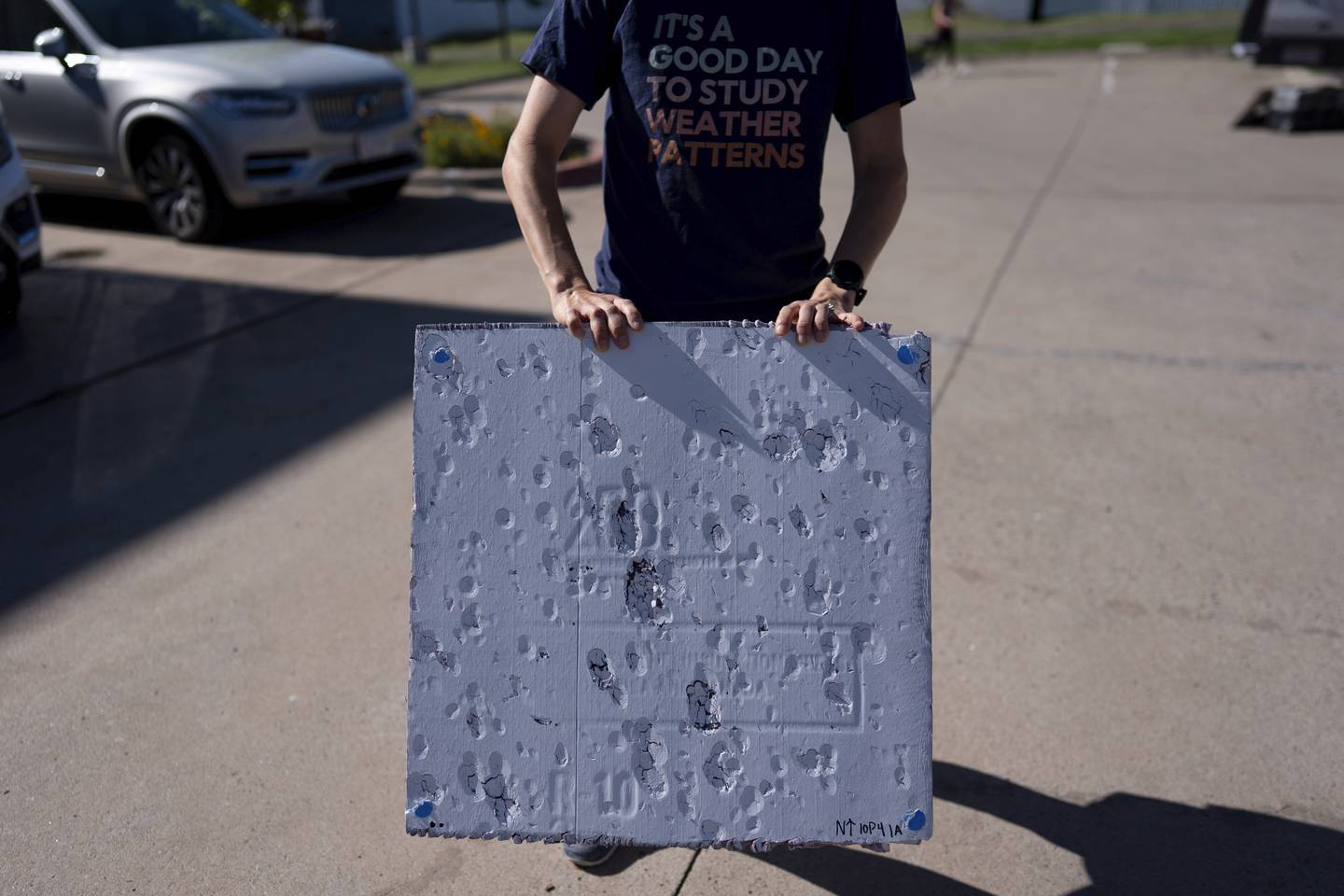 Hannah Vagasky holds a foam board hail pad covered with impact dents in a parking lot in Shamrock, Texas, as the team prepares for a day of hailstorm chasing. The hail pad is used to measure the size, angle of impact and intensity of hail.