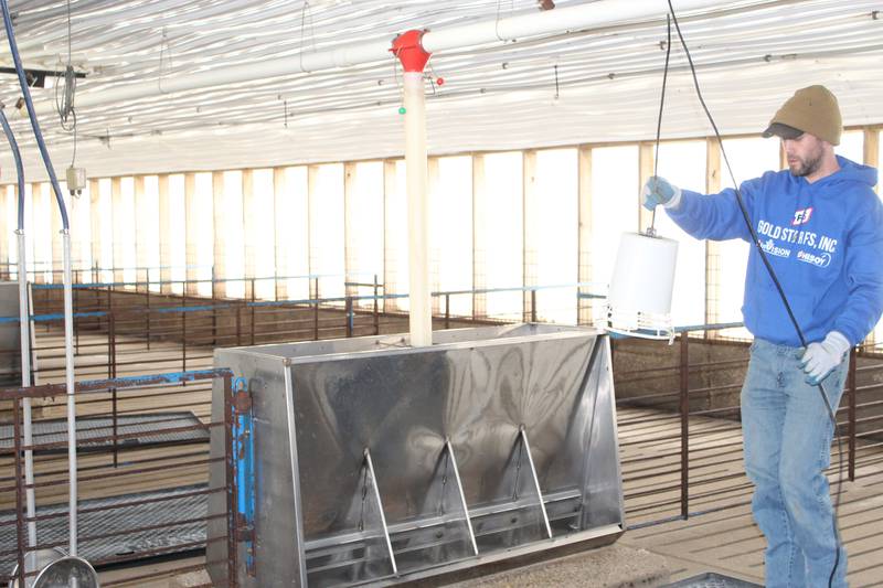 Chad Bell positions a heat lamp above the plastic mat that is in front of the feeder in his wean-to-finish barn in preparation for a new group of pigs. The mats will stay in the pens for about two weeks after the pigs arrive to provide them a warm place to huddle up.