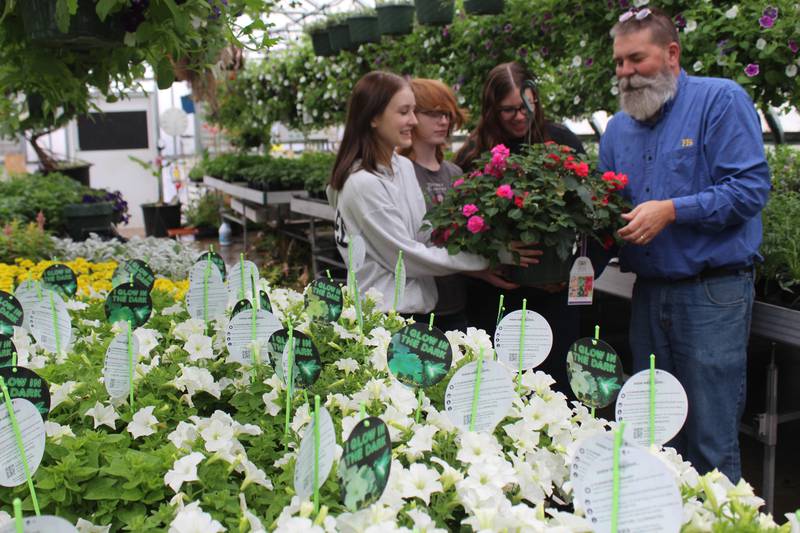 FFA adviser Joe Steffen (far right) and Newark FFA members Miranda McBroom (from left), Hannah Severson and Maddi Dierzen show one of the many hanging baskets that were available during the Newark FFA Greenhouse Sale.