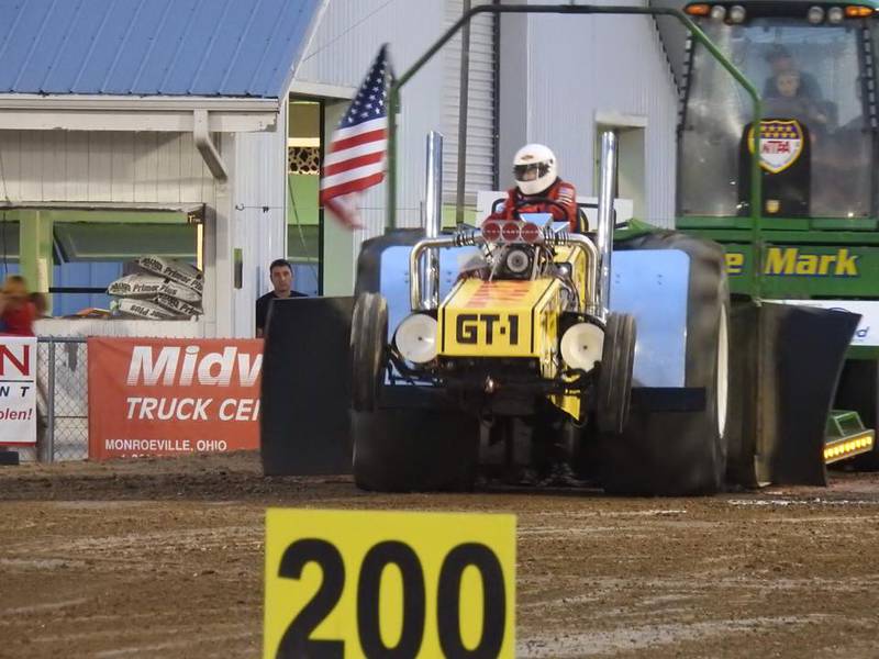 Larry McVey steers his Super Banana pulling tractor, a modified 1955 Massey Harris with a turbocharged Dodge Hemi engine, down the track at a National Tractor Pulling Legends tractor pull. McVey helped his father, Lloyd McVey Sr., build the pulling tractor in the early 1970s. The NTPL circuit features tractors and drivers from the early days of tractor pulling. The NTPL requires safety devices including kill switches, side shields and safety hitches. Their insurer does not require the use of roll cages.