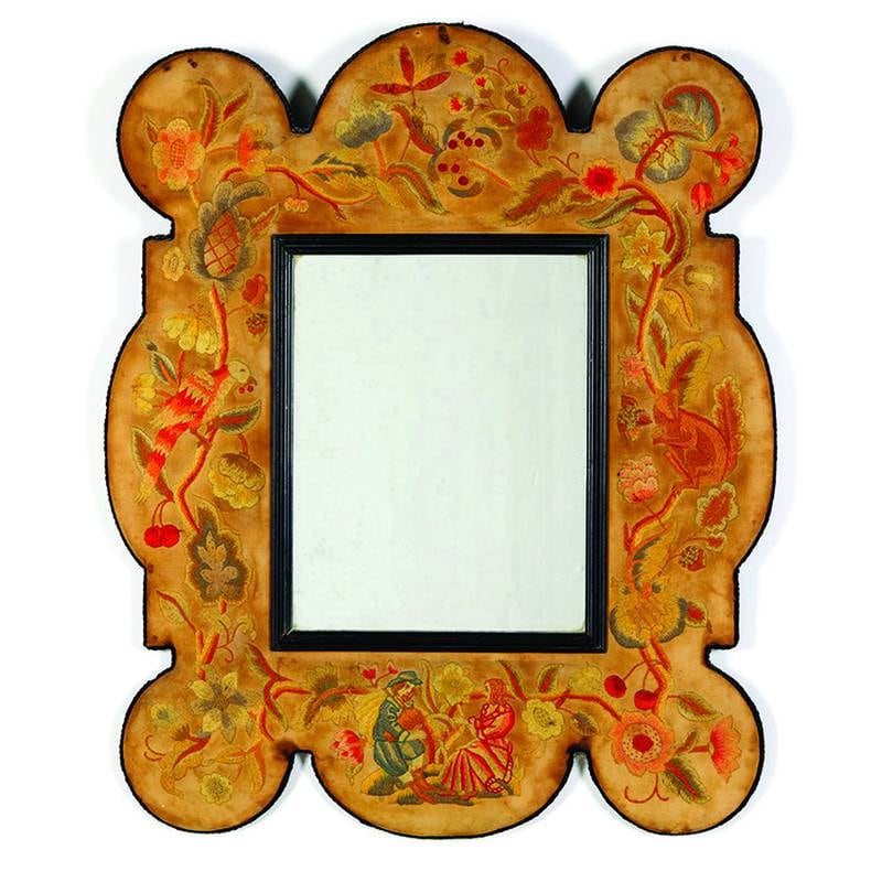 This mirror with an embroidered frame was made in the 20th century in the style of the William and Mary period.
