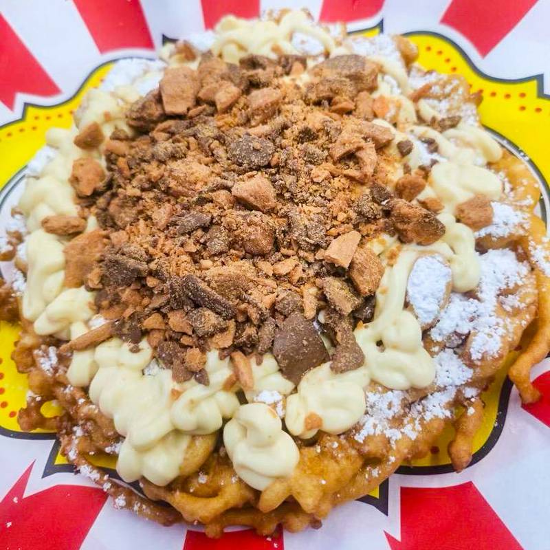 Butterfinger Funnel Cake by North American Midway Entertainment. Crispy, golden funnel cake topped with smooth vanilla cream and crunchy Butterfinger pieces. A perfect mix of sweet, creamy, and crunchy in every bite.