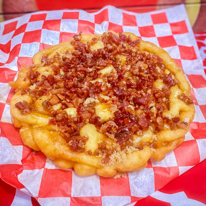 Piggy Funnel by R&W Concessions. Fluffy funnel cake drizzled with brown sugar and maple syrup, topped with bacon pieces.