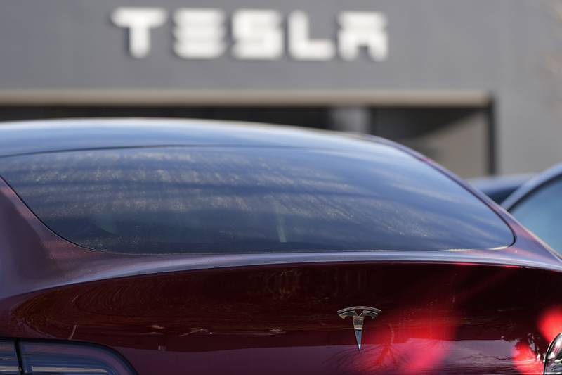 A Tesla model Y and other Telsla vehicles sit at a dealership.