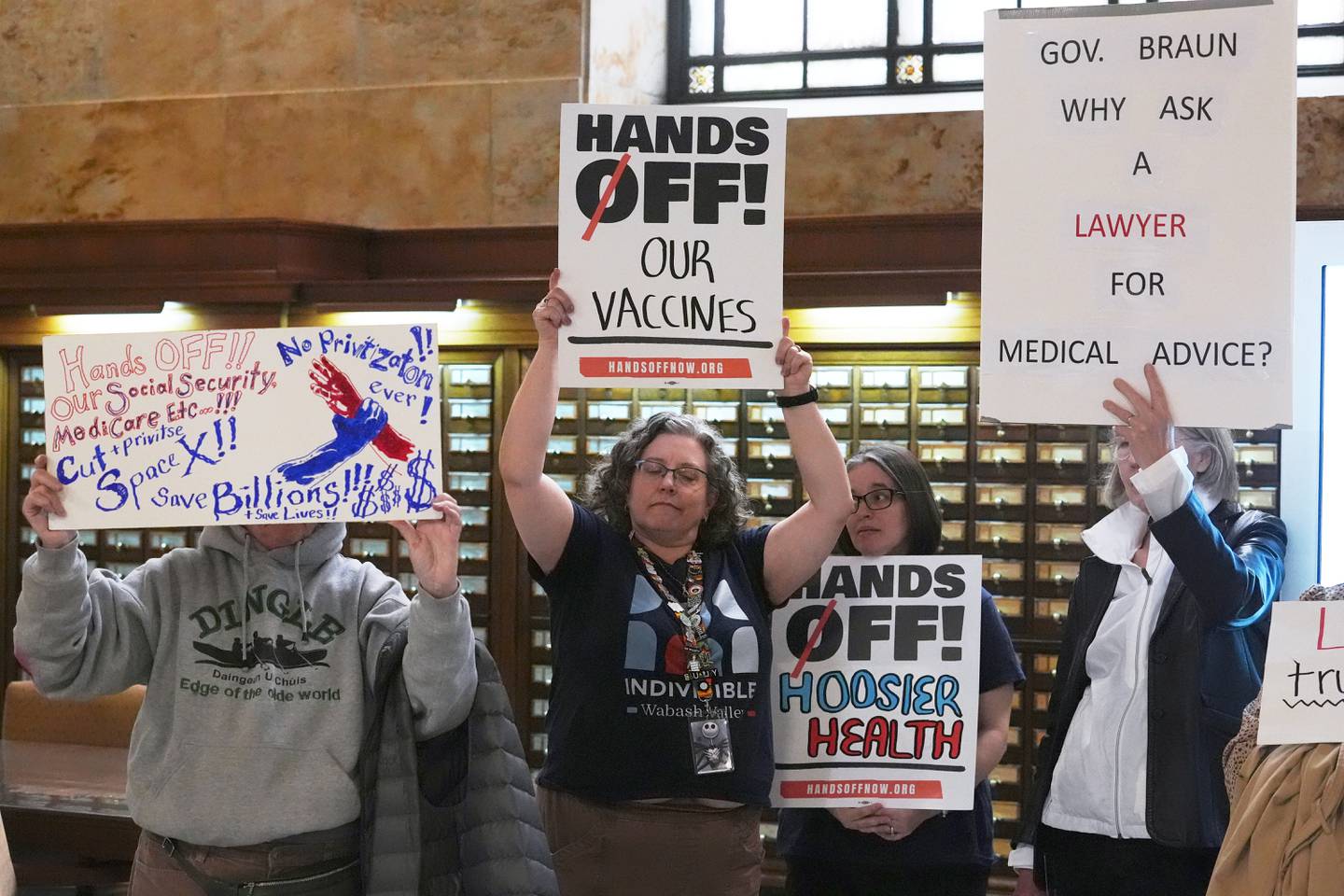 Protesters hold up signs outside of the Make Indiana Healthy Again initiative event in Indianapolis.