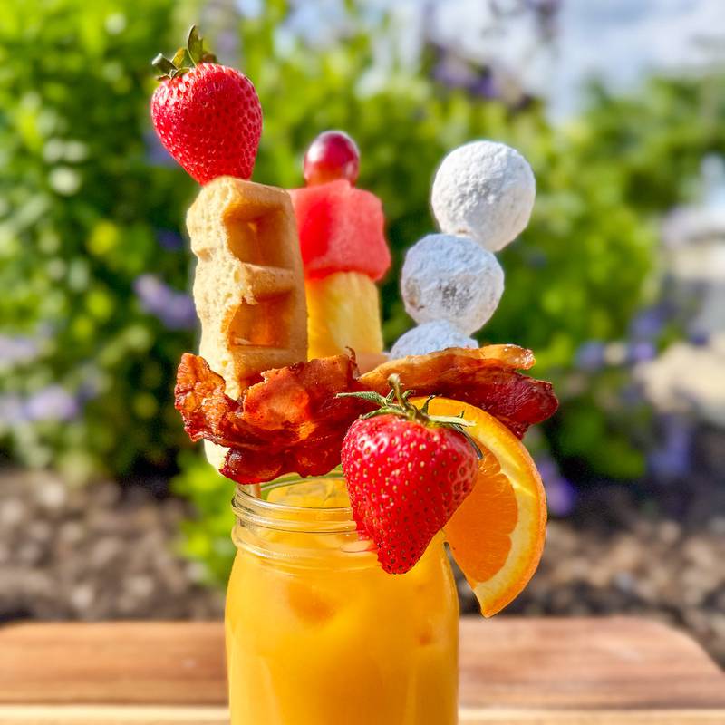 Brunch Mimosa by Urick Concessions. This isn't your average mimosa—served with skewers of a mini sausage breakfast sandwich, fruit kebab, crispy bacon, donut holes, and a waffle stick, it's brunch in a glass with a bubbly twist.