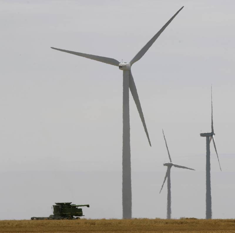 A combine is dwarfed by 262-foot-tall wind turbines. Since 2010, foreign renewable energy investments in U.S. agricultural land have increased by at least 10.4 million acres — a 353% rise, accounting for nearly half of the 21-million-acre total increase in foreign-owned ag land during this period.