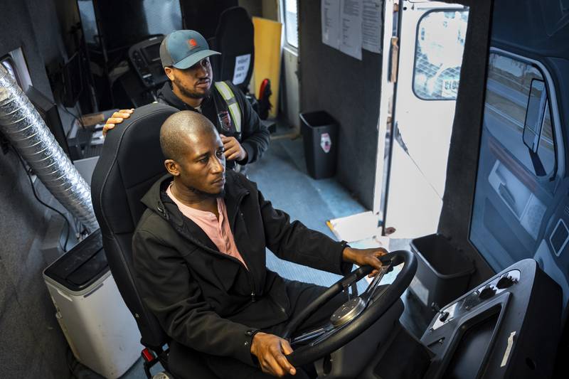 Trucking student Mohammed Kamal, overseen by instructor Tom Panton, practices driving a tractor-trailer truck in a simulation at the Driving Academy in Linden, New Jersey.