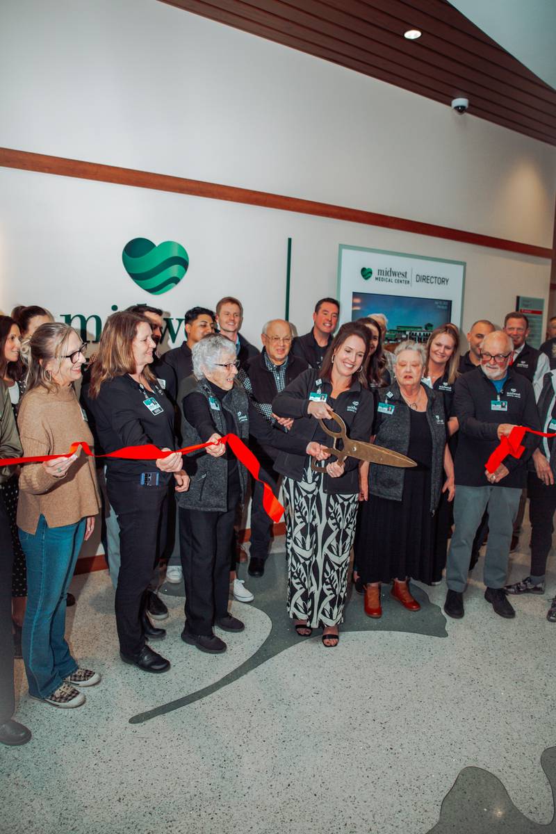 Surrounded by the board of directors and executive management team, Tracy Bauer, president and CEO of Midwest Medical Center, cuts the ribbon and marks the official expansion opening at the health care facility in Galena, Illinois.