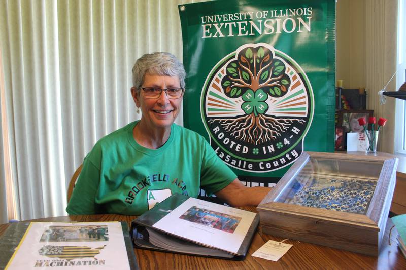 Terri Sancken shows her son Brent’s 4-H record books and his art project, which received a superior award at the Illinois State Fair. The logo for La Salle County 4-H on the banner behind Sancken was designed by Brent.