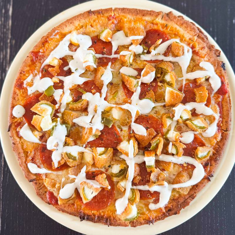Jalapeño Popper Pizza by DG Concessions/Ginocchios Pizza. They start with a garlic butter and light marinara base. Topped with a mozzarella cheese blend, pepperoni, jalapeno poppers, bacon, and finished with a drizzle of ranch dressing.