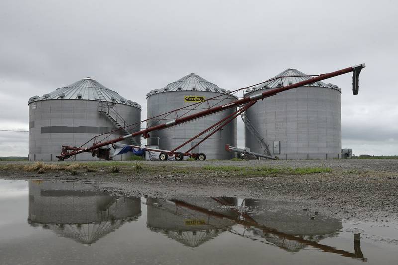 The image of grain storage bins and farm equipment is reflected in water.