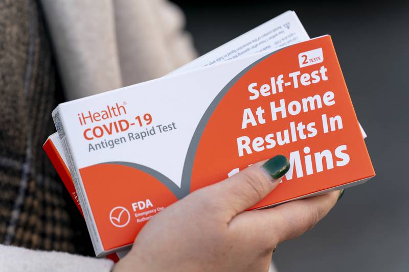 A woman holds two boxes of at-home COVID-19 test kits.