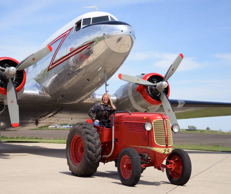 Sherry Schaefer sits in the seat of her 1944 Oliver Airport 25 in front of a 1944 airplane. Less than 150 of these tractors were built, making them a very rare tractor.