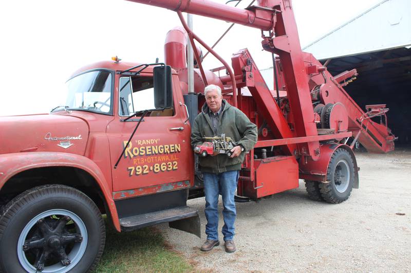 Randy Rosengren stands in front of his corn sheller that he purchased in 1982, while holding a replica of it. The corn shelling business has been a big part of the farmer’s life and it provided him with the opportunity to meet a lot of good farmers.