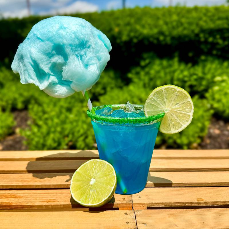 Blue Cotton Candy Margarita by Urick Concessions. A fun, vibrant cocktail that combines the tangy flavor of a classic margarita with the sweet, whimsical taste of cotton candy. Made with tequila, blue curaçao, lime juice, and a touch of real cotton candy for garnish of sweetness.