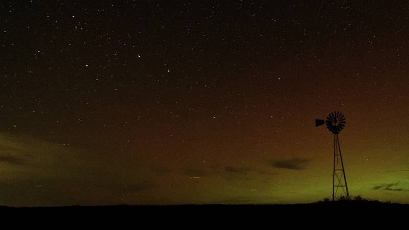 An aurora borealis, also known as the northern lights, is seen in the night sky with the Big Dipper constellation behind a windmill water pump.