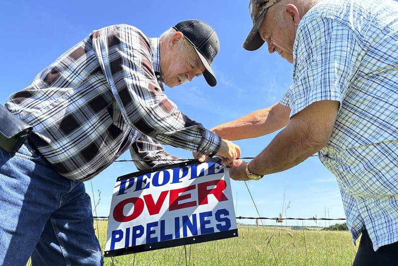 Gaylen Dewing (left) and Marvin Abraham affix a sign to a roadside fence east of Bismarck, North Dakota. The sign reads “People over Pipelines” and is in opposition to Summit Carbon Solutions’ proposed five-state, 2,000-mile pipeline network to carry carbon dioxide emissions from dozens of Midwestern ethanol plants to North Dakota for permanent storage deep underground.