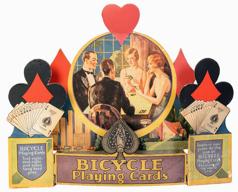 When advertisements include pictures of people, their clothing and hairstyles can help date the item. This store display for Bicycle Playing Cards is from about 1930.