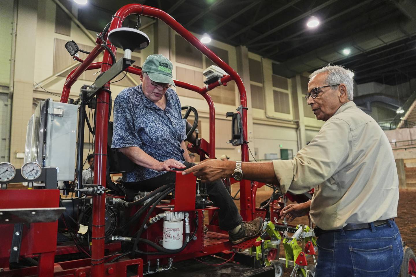 Farmer Vicki Morrane (left) listens as Ajit Srivastava (right) explains the mechanics of an electric tractor before she test drives in East Lansing in Michigan’s Lower Peninsula.