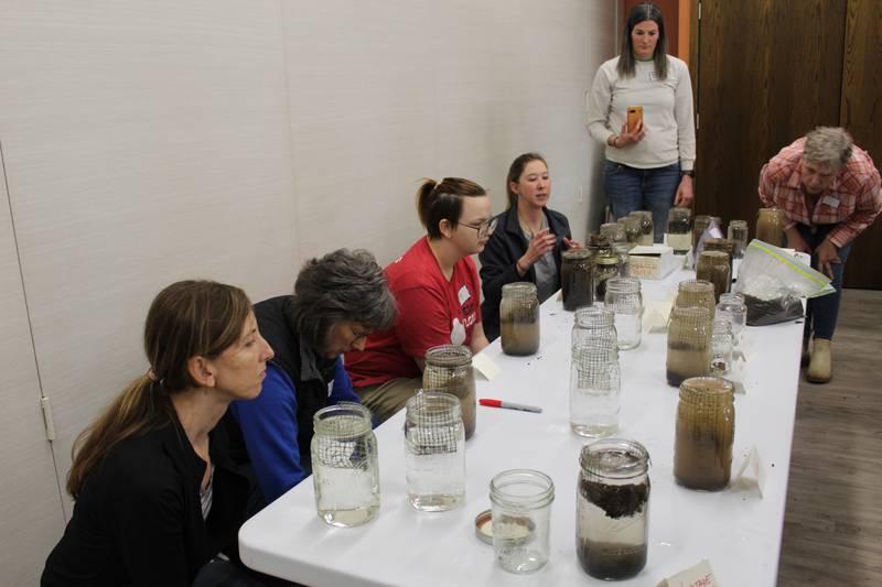 Ladies evaluate soil from their farms with a slake test during a Learning Circle meeting. Using a clear jar with a wire mesh to suspend the soil sample, water is added to evaluate the stability of the soil aggregates.