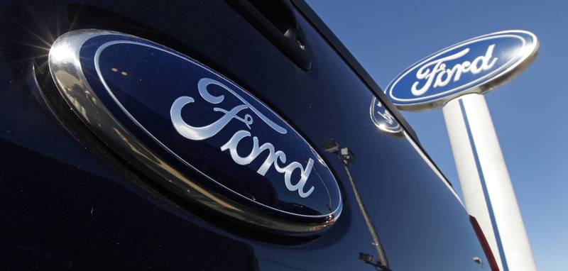 A Ford logo is on the tailgate of a pickup truck and on a Ford dealership sign in Salem, New Hampshire.