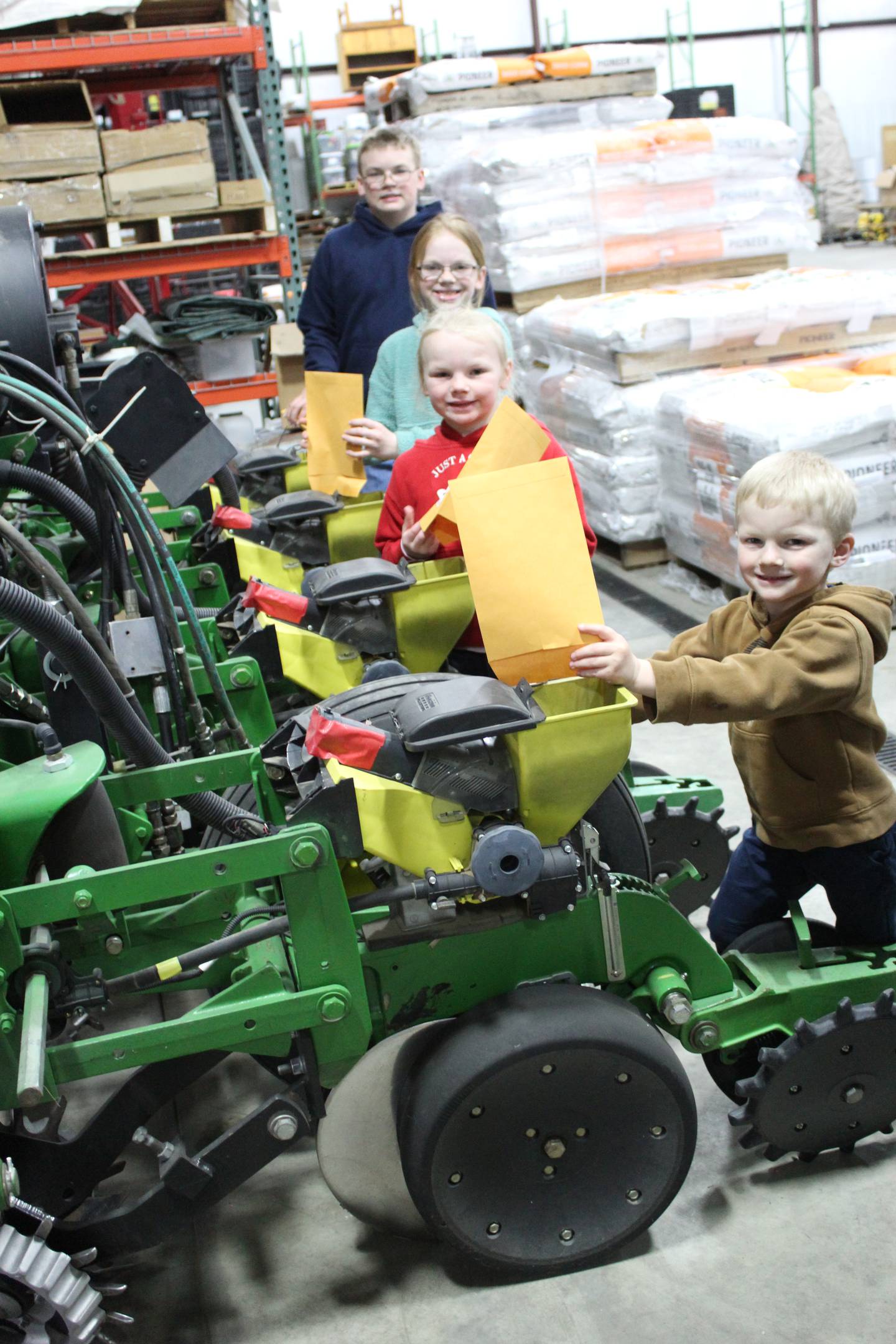 Correy and Kellie Rahn’s kids Anthony (from front to back), Adalynn, Emilie and Austin demonstrate how they add seed to the boxes of the four-row test plot planter. The kids help fill these envelopes in the seed shed in advance to help speed up the planting process in the field.