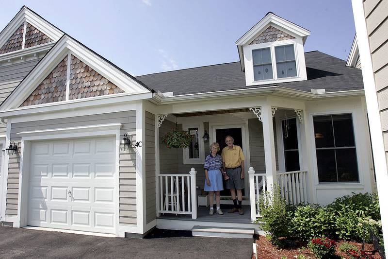 A couple stands on the porch of their home at The Villages at Quail Run, an age-restricted housing community for people age 55 and over, in Hudson, Massachusetts.
